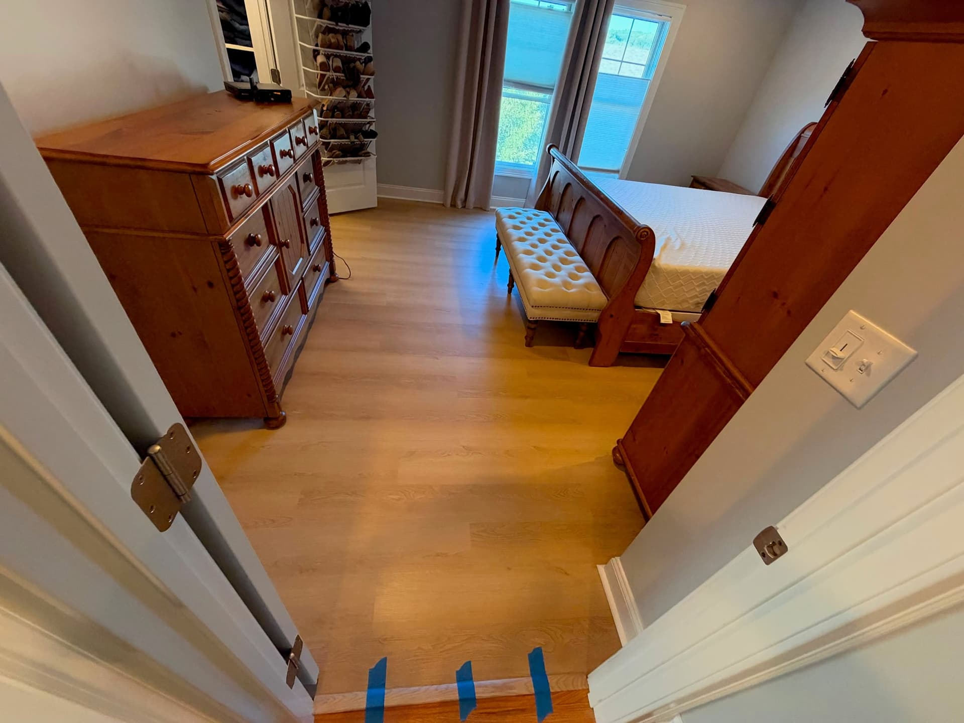 White Sand LVP at a Newington bedroom doorway with wood furniture beyond and temporary blue painter's tape at the threshold