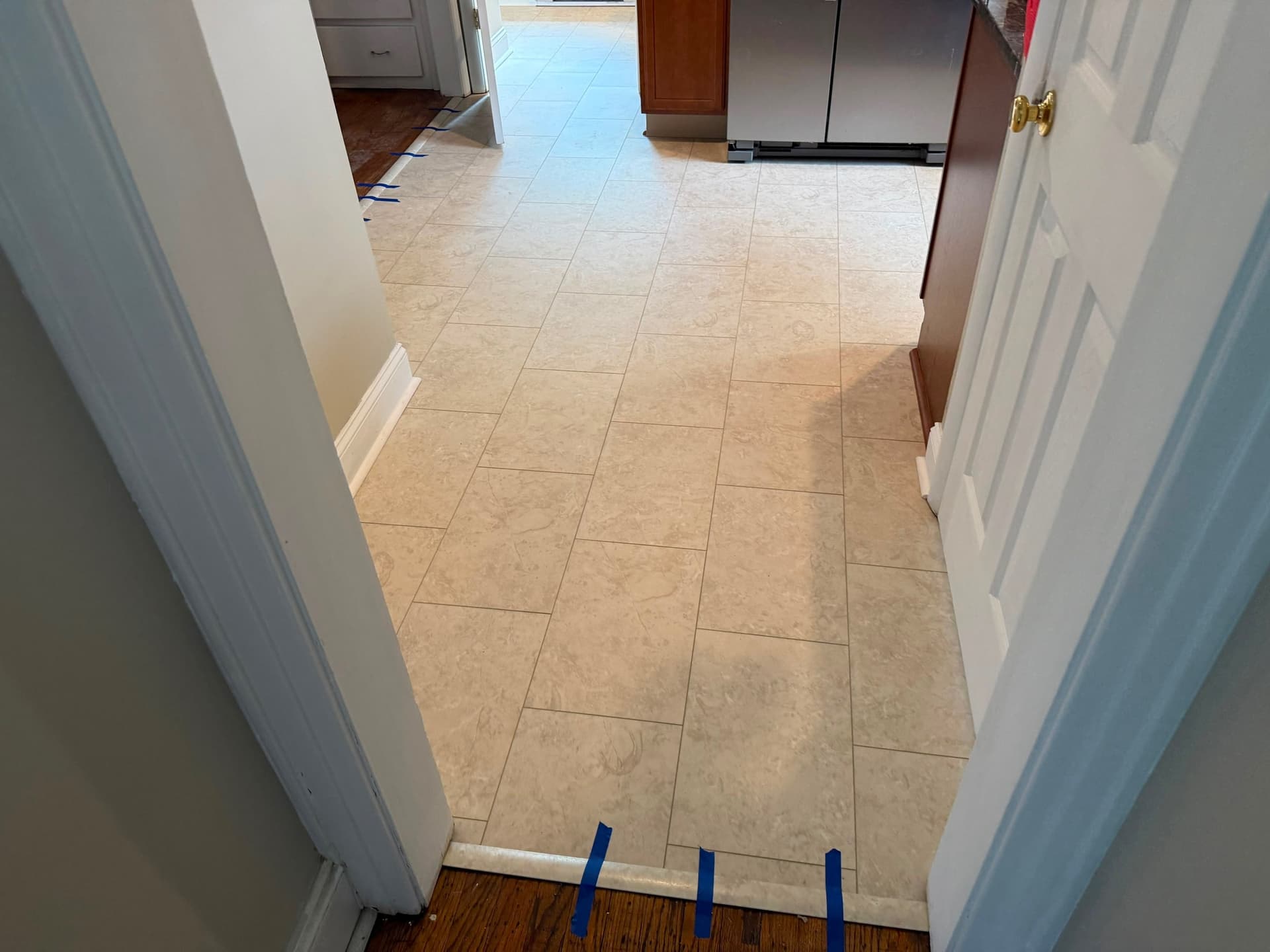 Completed kitchen LVT meeting hardwood at doorway transitions with blue tape visible on the transition pieces