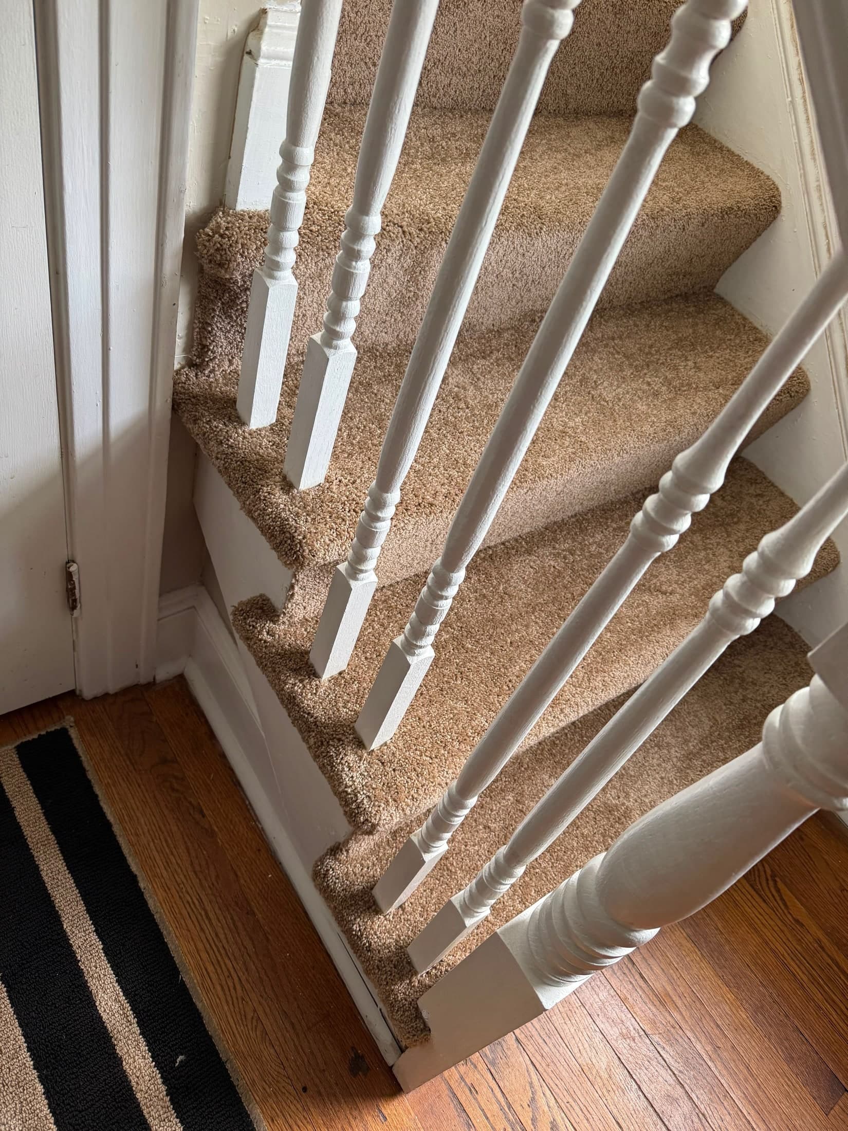 Close view of tan stair carpet fitted around white railing spindles and exposed stair edges