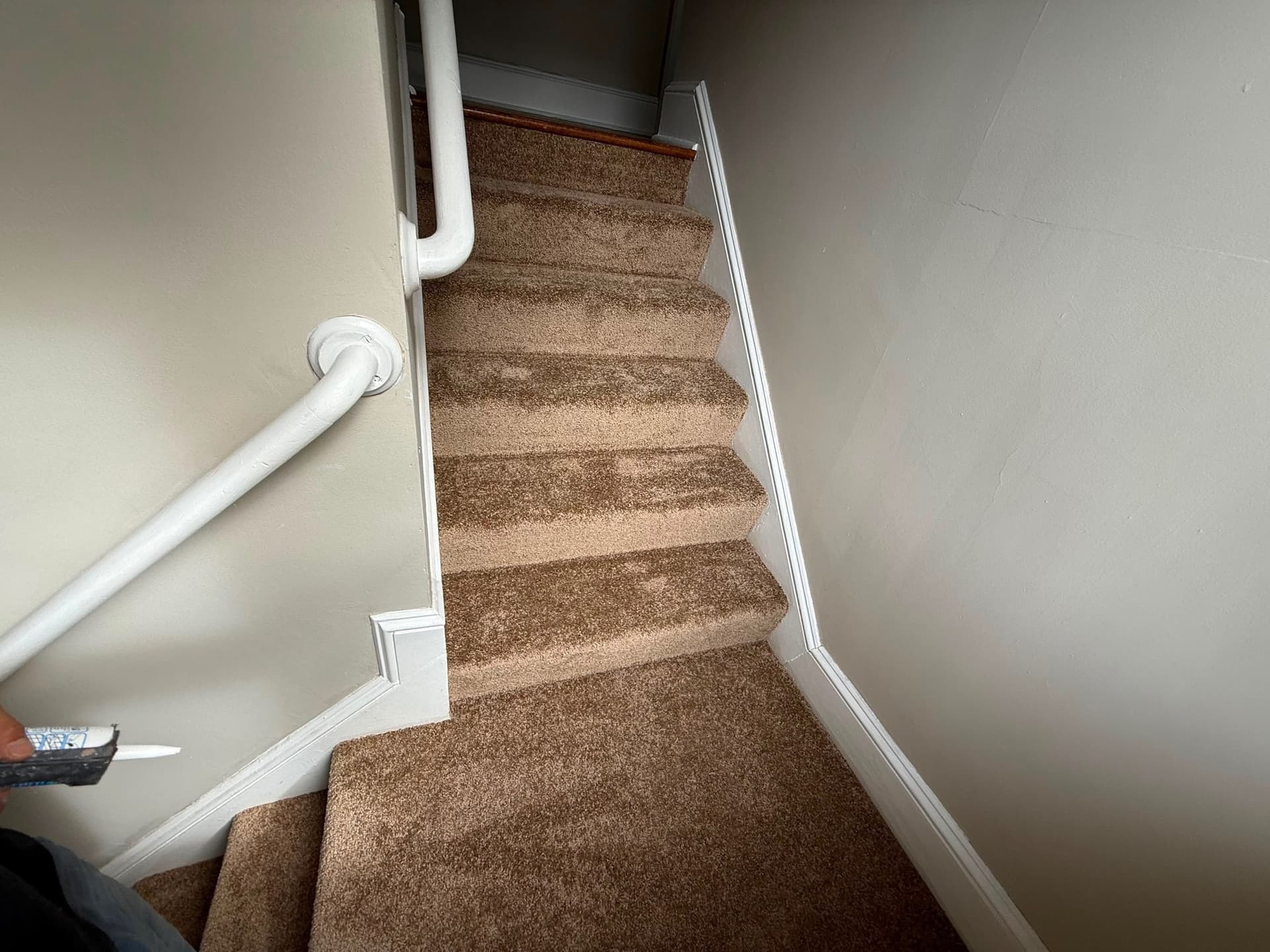 Tan textured carpet fitted on the upper stairs and turning treads between painted walls and white handrails